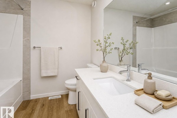 A bathroom with a white vanity, toilet, bathtub, and wood-look flooring. - 19 Parker Ln, Spruce Grove