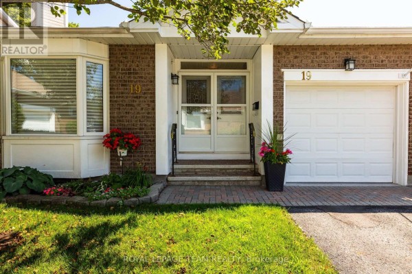Close-up exterior view of the townhouse entrance with brick facade and white garage door. - 19 Pine Needles Court, Ottawa