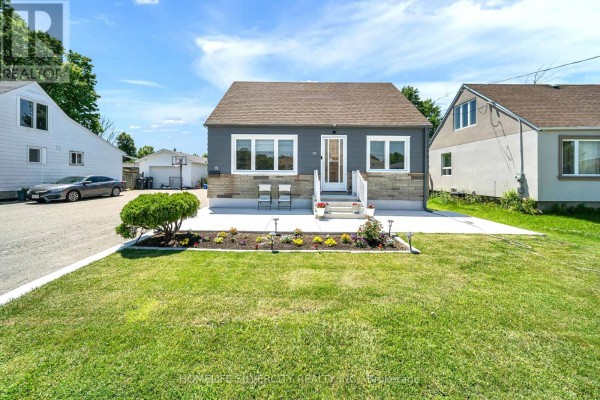 A sunlit view of the bungalow's front facade, showing a concrete patio and landscaping. - 19 Pleasantview Avenue, Brampton