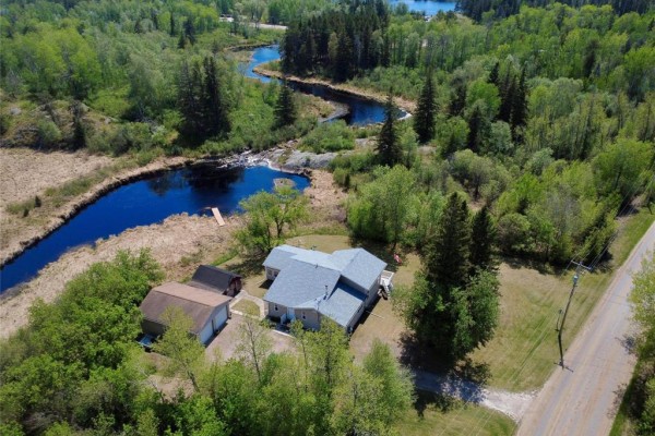 Aerial view of a beige house and garage in a wooded area with a winding river and lake. - 19 Rink Road, Rennie