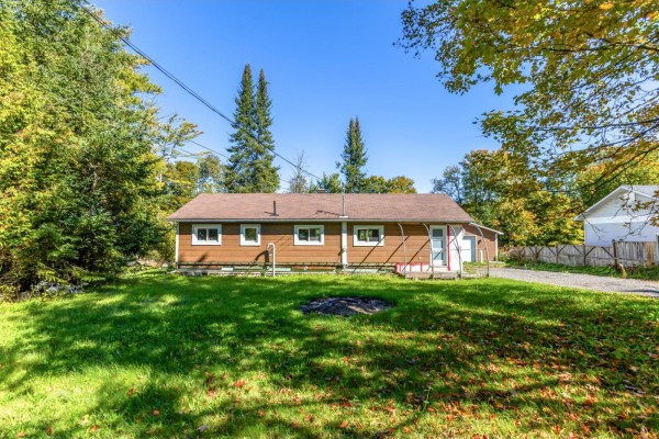 Rear view of a one-story brown house with white windows and a red-trimmed door, surrounded by green grass. - 19 Rue Du Centre, Val Des Monts