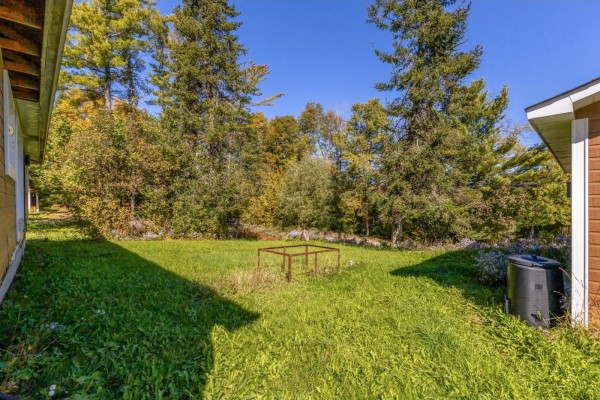 A grassy backyard with a metal fire pit structure in the center and mature trees in the background. - 19 Rue Du Centre, Val Des Monts