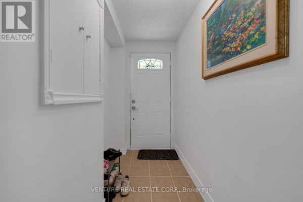 Interior entryway with a white door, beige tiled floor, and artwork on the wall. - 19 Spadina Road, Brampton