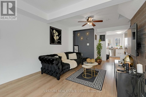 Living room with a black tufted sofa, coffee tables, and a view of the kitchen. - 19 Spadina Road, Brampton