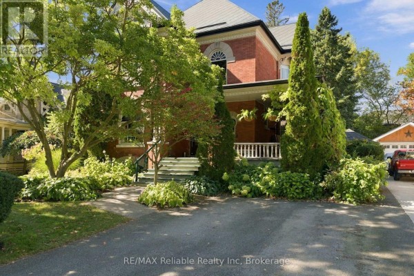 Front view of a brick house with a covered porch, staircase, and manicured shrubs. - 19 Sparling Street, Huron East