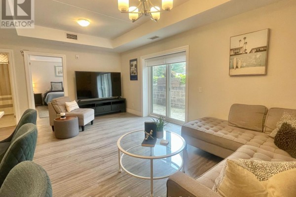 Living room area with a large sectional sofa, television, and a sliding glass door leading to an outdoor patio. - 101 - 19 Stumpf Street, Centre Wellington
