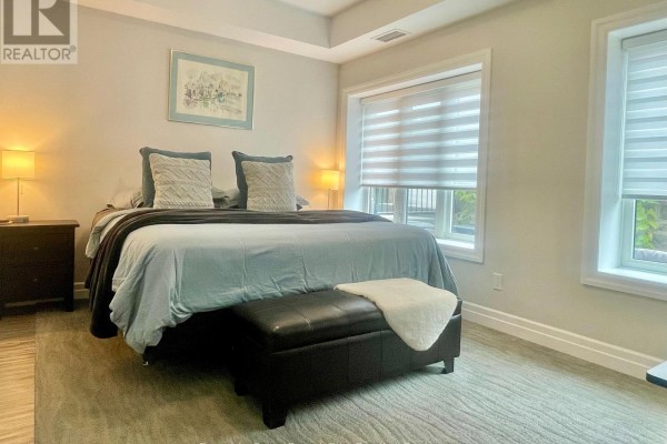 Bedroom with a king-size bed, nightstands, dresser, and large windows with blinds offering natural light. - 101 - 19 Stumpf Street, Centre Wellington