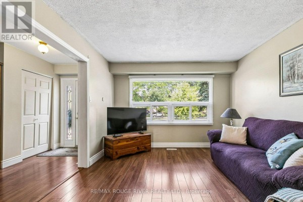Living room with dark wood floors, purple sofa, television, and window overlooking greenery. - 19 Tinbury Place, Toronto