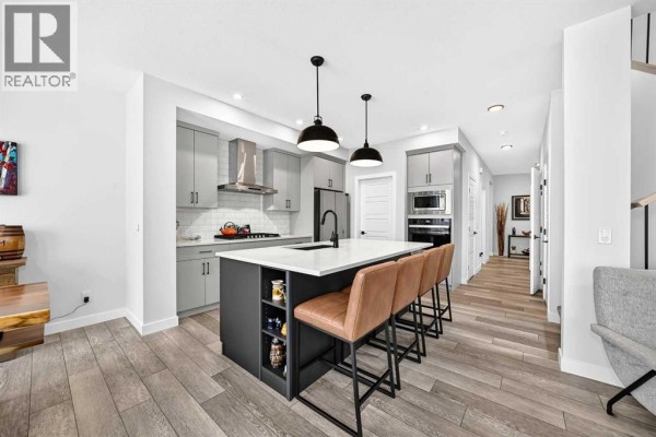 Kitchen and dining area with grey cabinets, white subway tile backsplash, and wooden floors. - 19 Versant View Sw, Calgary