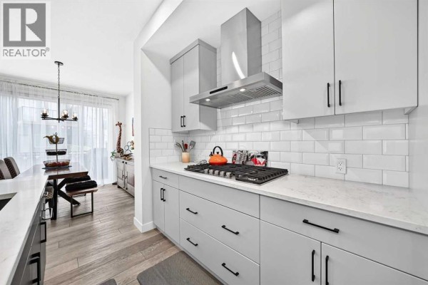 Close-up of the kitchen with a gas range, stainless steel hood fan, and grey cabinets. - 19 Versant View Sw, Calgary