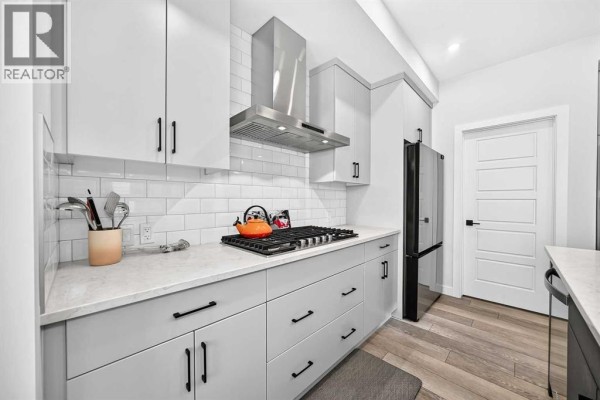 Kitchen area showing a stainless steel refrigerator, grey cabinets, and white subway tile backsplash. - 19 Versant View Sw, Calgary