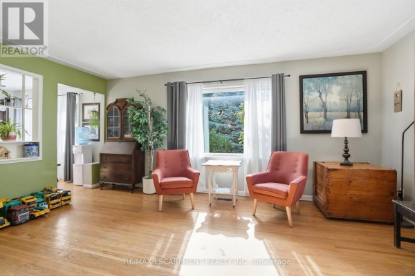 Living room with two orange chairs, a wooden desk, and a large window. - 19 Victoria Street, Brant