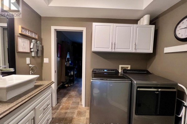 Kitchen with dark brown cabinets, wooden countertops, and beige tiled floor. Stainless steel sink and window with blinds. - 19 Wolf Street, Tillsonburg