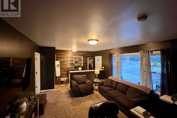 Living room with dark brown furniture, carpeted floor, and a dark accent wall with wood paneling. - 19 Wolf Street, Tillsonburg