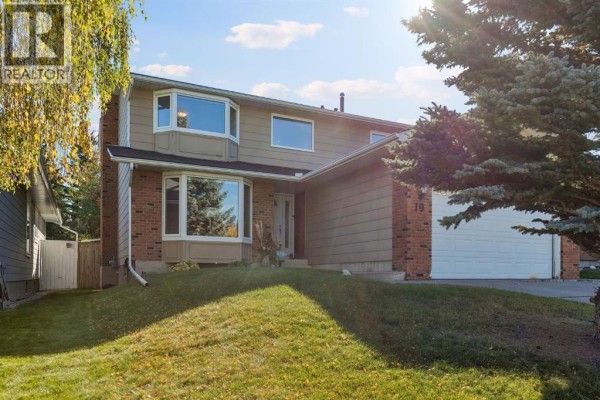 Front exterior of a house with bay windows, brick and tan siding, and a sloped lawn. - 19 Woodbrook Road Sw, Calgary