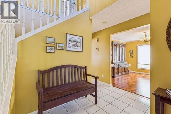 Foyer with yellow walls, white tiled floor, wooden bench, and staircase with white railing. - 19 Woodbrook Road Sw, Calgary