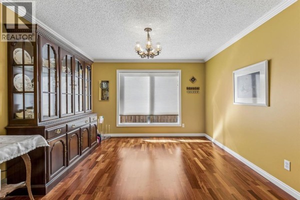 Dining room with yellow walls, hardwood floors, large china cabinet, window, and chandelier. - 19 Woodbrook Road Sw, Calgary
