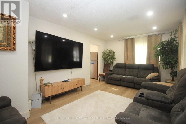 Living room with a large TV, sectional sofa, rug, and light wood floors. - 190 Helena Avenue, London South