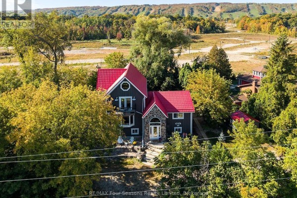 Exterior view of a dark grey house with a red metal roof, stone accents, and mature trees in the foreground. - 190 Lakeshore Road E, Blue Mountains