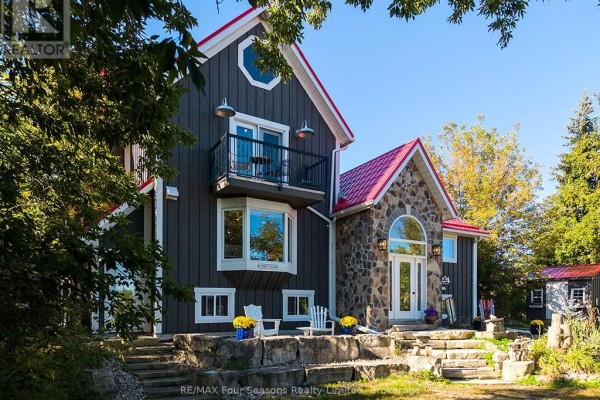 Close-up exterior view of a grey house with a red roof, stone facade, arched entryway, and a balcony with railing. - 190 Lakeshore Road E, Blue Mountains