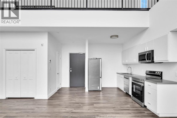 Living area and kitchen with stainless steel appliances, white cabinets, and grey wood floors. Double doors on left. - 1900 6th Concession Unit# 403, Lasalle