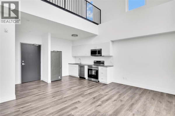 Open-concept living area and kitchen with stainless steel appliances, white cabinets, and grey wood floors. View of loft. - 1900 6th Concession Unit# 403, Lasalle