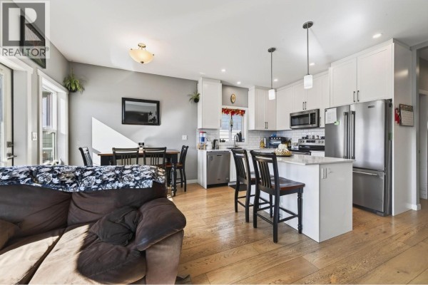 Open-concept living and kitchen area with white cabinets, stainless steel appliances, and a dark sofa. - 1900 Ord Road Unit# 21, Kamloops