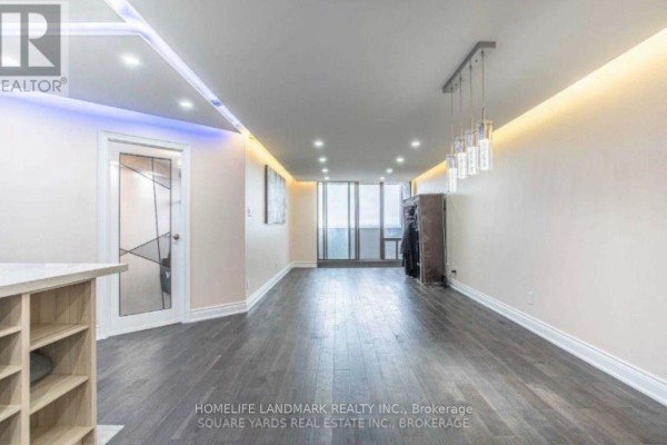 Spacious living room with dark wood floors, tray ceiling lighting, and a large window. - 1901 - 10 Tangreen Court, Toronto