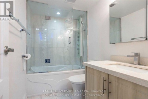 Bathroom with a white bathtub, glass shower doors, toilet, and wood-look vanity. - 1901 - 10 Tangreen Court, Toronto