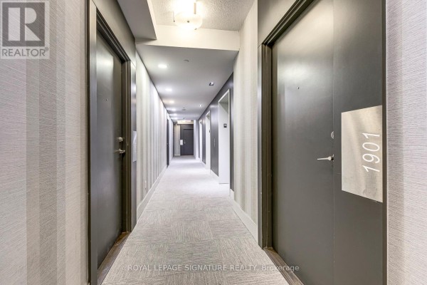 A long, carpeted apartment hallway with grey doors and patterned wallpaper. - 1901 - 20 Bruyeres Mews, Toronto