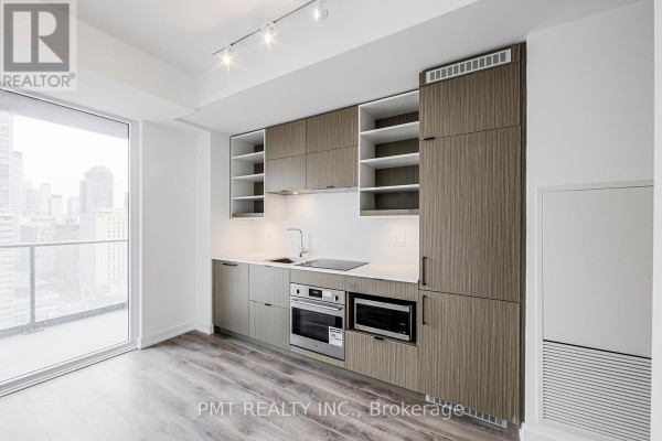 Compact kitchen with light wood cabinetry, white countertops, and stainless steel appliances. - 1901 - 20 Edward Street, Toronto