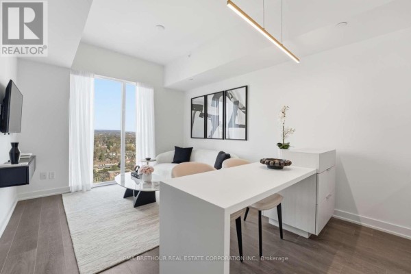 Apartment living space with large window, white sofa, and modern kitchen island with stools. - 1901 - 370 Martha Street, Burlington