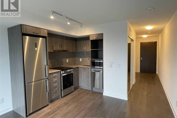Modern apartment kitchen with stainless steel appliances and grey cabinetry, leading to a hallway. - 1902 - 219 Dundas Street E, Toronto