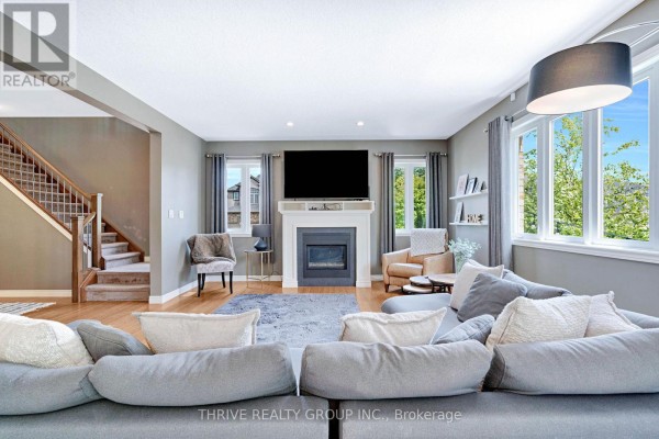 Open-concept living room with a grey sectional sofa, large windows, and a view into the dark wood kitchen and dining area. - 1903 Jubilee Crescent, London North