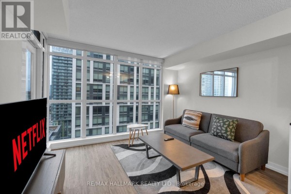 Living room with a grey sofa, coffee table, rug, and large windows overlooking the city. - 1905 - 151 Dan Leckie Way, Toronto