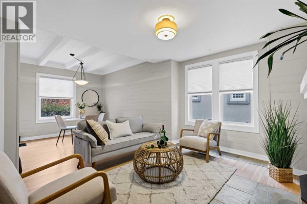 Living room with light gray walls, white brick fireplace, and two gray sofas with wooden chairs. - 1905 2 Street Nw, Calgary