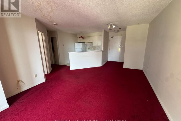 Living area with red carpet, opening to a small kitchen with white cabinets. - 1906 - 25 Grenville Street, Toronto