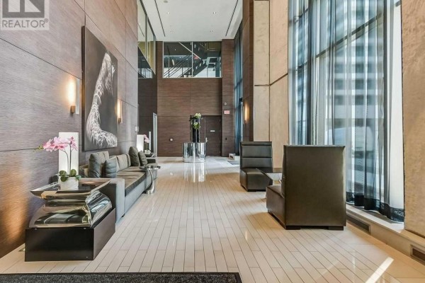 Luxurious building lobby with wood-paneled walls, marble floors, modern seating, and a tall window. - 1906 - 33 Shore Breeze Drive, Toronto