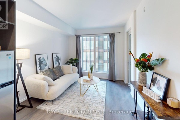 Living area with sofa, coffee table, kitchen appliances, and a large window. - 1906 - 68 Shuter Street, Toronto