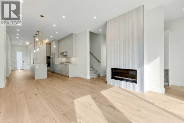 Open concept living room with light wood floors, a gas fireplace, and a staircase. - 1906 5 Street Ne, Calgary