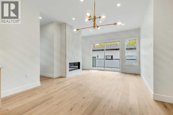 Living room with light wood floors, a gas fireplace, and sliding glass doors to a balcony. - 1906 5 Street Ne, Calgary