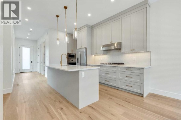 Modern kitchen with light gray cabinets, a large island, stainless steel appliances, and pendant lighting. - 1906 5 Street Ne, Calgary