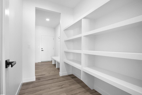 Walk-in pantry with extensive white shelving, wood-look flooring, and a bench. - 19066 20a Av Nw, Edmonton