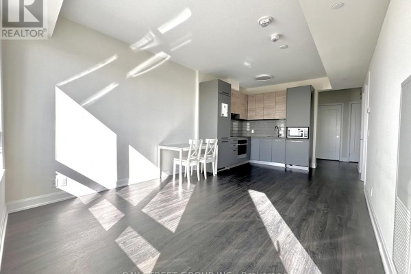 Interior view of a studio apartment showing a compact grey kitchen, a small dining table, and dark wood flooring. - 1907 - 38 Gandhi Lane, Markham