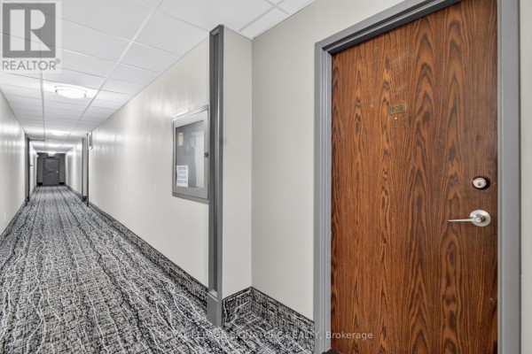 Long hallway with patterned carpet, white walls, and a wooden apartment door. - 1908 - 25 Kensington Road, Brampton