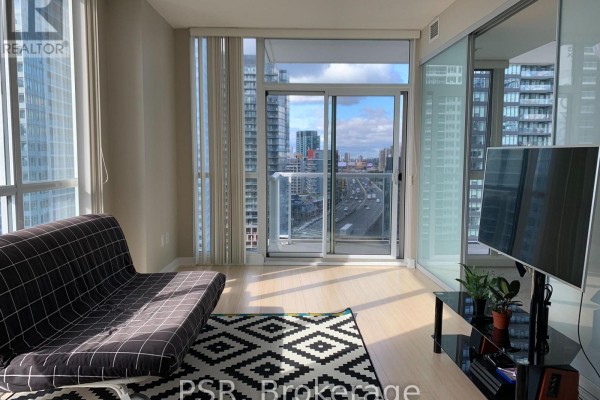 Living area with sofa, patterned rug, and large windows overlooking the city skyline. - 1908 - 75 Queens Wharf Road, Toronto