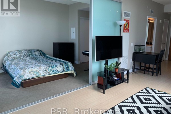 Bedroom area with a bed, sliding glass door partition, and living area view. - 1908 - 75 Queens Wharf Road, Toronto