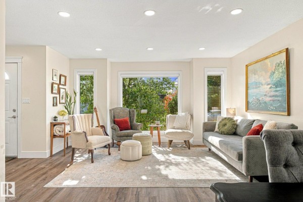 Living room and entryway with beige walls, wood flooring, and a large area rug. - 1908 36 Av Nw, Edmonton