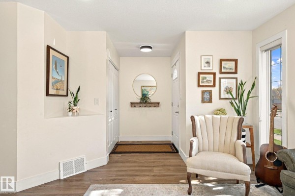 Entryway with beige walls, wood flooring, a round mirror, and artwork on the walls. - 1908 36 Av Nw, Edmonton