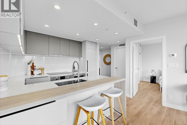 Kitchen with white countertops, grey cabinets, stainless steel appliances, island with bar stools, and doorway to bedroom. - 1909 567 Emerson Street, Coquitlam